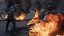 Seorang pria mengendarai motor saat pengunjuk rasa anti-pemerintah membakar ban untuk memblokir jalan di Beirut, Selasa (2/3/2021). Warga Lebanon yang marah memblokir jalan di seluruh negeri dengan membakar ban setelah mata uang Lebanon jatuh ke titik terendah baru. (AP Photo/Hassan Ammar)