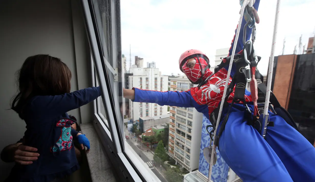 Petugas pembersih kaca berkostum Spiderman bercanda dengan seorang pasien anak yang dirawat di RS Infantil Sabara, Sao Paulo, Senin (10/10). Aksi ini bagian dari perayaan Hari Anak Brasil yang diperingati setiap 12 Oktober. (REUTERS/Paulo Whitaker)