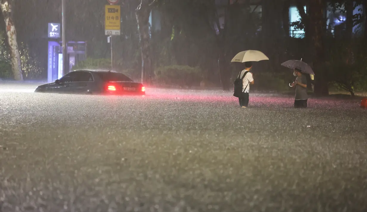 Orang-orang melihat mobil yang terendam banjir di jalan selama hujan lebat di distrik Gangnam, Seoul, Korea Selatan pada 8 Agustus 2022. Markas Besar Penanggulangan Bencana dan Keselamatan Pusat menaikkan peringatan krisis ke tingkat tertinggi dan meminta organisasi publik dan swasta untuk menyesuaikan jam kerja mereka. (Photo by YONHAP / AFP)