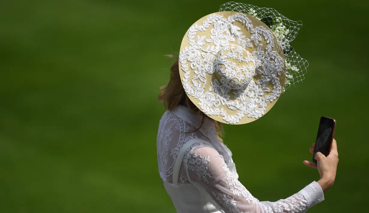 Seorang penonton balap berswafoto saat menghadiri hari pertama balap kuda Royal Ascot, di Ascot, barat London Selasa (15/6/2021). Balap kuda eksklusif yang hanya dihadiri oleh kalangan elit Inggris itu menjadi tradisi tahunan sejak tahun 1711. (DANIEL LEAL-OLIVAS / AFP)