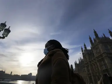 Seorang perempuan yang mengenakan masker melintasi Jembatan Westminster di London, Kamis (9/12/2021). Perdana Menteri Inggris Boris Johnson telah mengumumkan pembatasan yang lebih ketat untuk membendung penyebaran varian baru Covid-19, omicron. (AP Photo/Frank Augstein)