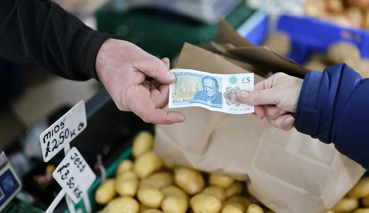 Seorang pelanggan memberikan uang kertas lima pound kepada pemilik kios untuk membayar buah dan sayuran di Walthamstow Market, London, Minggu (22/11/2021). Inflasi Inggris telah mencapai level tertinggi 10 tahun karena tagihan energi rumah tangga meroket, menurut data minggu lalu. (Tolga Akmen/AFP)