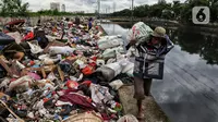 Warga membawa sampah sisa banjir yang dikumpulkan dari sepanjang Kali Cengkareng, Jakarta Barat, Kamis (9/1/2020). Tumpukan sampah di sepanjang bantaran kali dan rumah-rumah warga terlihat setelah banjir yang melanda sejumlah kawasan Jakarta mulai surut. (Liputan6.com/Johan Tallo)