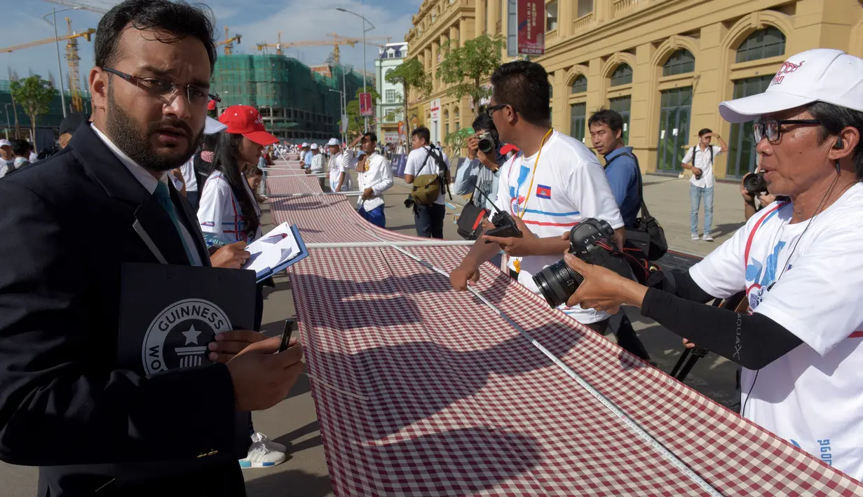 Juri Guinness, Swapnil Dangarikar menyaksikan pengukuran syal tenun tangan yang dikenal sebagai Krama pada upaya pemecahan rekor di Phnom Penh, Kamboja, Minggu (1/7). Syal krama di Kamboja masuk dalam buku Guinness World Records. (AFP/TANG CHHIN Sothy)