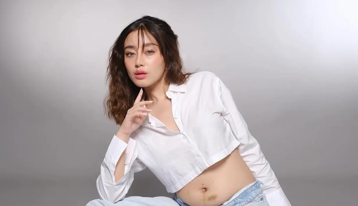 Tasya tampil menawan dengan balutan kemeja putih crop top dan celana jeans longgar. Dengan pose santai di lantai, ia memancarkan kebahagiaan dan kebanggaan atas kehamilan keduanya. Senyumnya yang lembut semakin menambah aura kehangatan dalam foto tersebut. (Liputan6.com/IG/@tasyarevina)