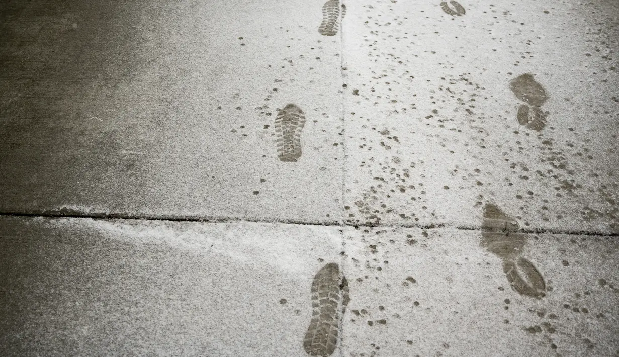 Jejak kaki di Main Street saat salju turun di Ann Arbor, Michigan, Rabu (2/2/2022). Badai salju membuat maskapai membatalkan ratusan penerbangan. (Jacob Hamilton/Ann Arbor News via AP)