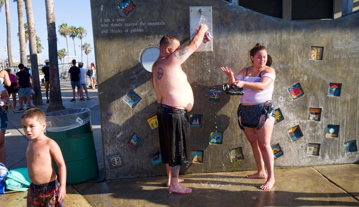 Anggota keluarga mendinginkan diri dengan mandi di pancuran luar ruangan di Venice Beach, Los Angeles, Amerika Serikat, Selasa (24/7). Panas ekstrem menyebar di seluruh Southwest. (AP Photo/Richard Vogel)