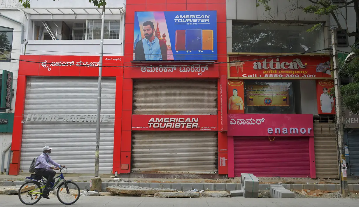 Seorang pria bersepeda di depan toko-toko yang tutup di area komersial saat pemberlakukan lockdown di Bangalore, Rabu (15/7/2020). Pusat IT India, Bangalore, kembali memberlakukan lockdown selama seminggu dimulai dari 14 Juli 2020 setelah adanya lonjakan kasus Covid-19. (Manjunath Kiran/AFP)