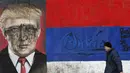 Seorang pria melintas di depan grafiti bergambar Presiden AS terpilih Donald Trump yang dirusak dengan cat di Belgrade, Serbia, Jumat (20/1). Trump hari ini akan dilantik menjadi Presiden AS. (AP Photo / Darko Vojinovic) 
