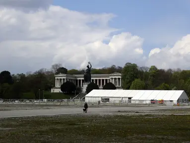 Seorang wanita dan anjingnya berjalan-jalan di Theresienwiese, area Festival bir Oktoberfest, di depan patung Bavaria dan pusat uji coba corona di Munich, Senin (3/5/2021). Jerman kembali membatalkan festival bir Oktoberfest untuk tahun kedua karena pandemi covid-19. (AP Photo/Matthias Schrader)