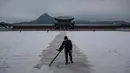 Seorang pekerja membersihkan salju di sebuah halaman di istana Gyeongbokgung selama hujan salju di pusat kota Seoul, Korea Selatan (13/12). (AFP Photo/Ed Jones)