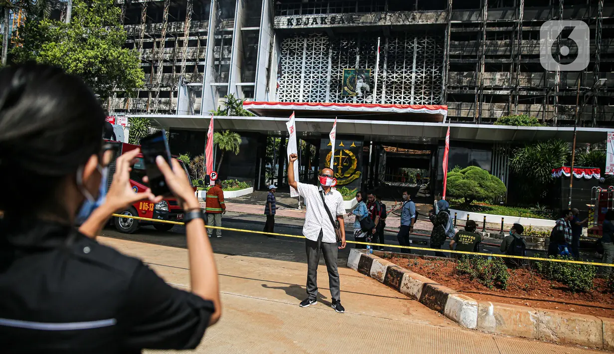 Seorang pria berfoto dengan latar belakang gedung utama Kejaksaan Agung RI yang terbakar di Jalan Sultan Hasanuddin, Jakarta, Minggu (23/8/2020). Banyak warga yang memadati Jalan Hasanuddin untuk melihat langsung kondisi gedung Kejaksaan Agung yang hangus dilalap api. (Liputan6.com/Faizal Fanani)