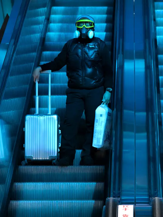 Seorang pelancong yang mengenakan masker untuk melindungi dari penyebaran virus korona menaiki eskalator di bawah jendela atap berwarna di Stasiun Kereta Api Beijing di Beijing, Kamis (28/1/2021).  Upaya untuk mencegah warga Tiongkok bepergian untuk Tahun Baru Imlek tampaknya berhasil. (AP Photo/Mar