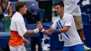 Petenis Serbia, Novak Djokovic berjabat tangan dengan Pablo Carreno Busta dari Spanyol usai gagal pada putaran keempat US Open 2020, di Flushing Meadows, (6/9/2020). Djokovic didiskualifikasi dari AS Terbuka 2020 setelah secara tidak sengaja memukul hakim garis dengan bola. (AP Photo/Seth Wenig)
