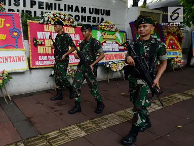 Sejumlah tentara bersenjata berjalan melintasi karangan bunga yang ada di Gedung Komisi Pemilihan Umum (KPU), Jakarta, Sabtu (20/4). Karangan bunga terus berdatangan ke Gedung KPU. (merdeka.com/Imam Buhori)