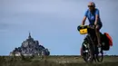 Seorang pria mengendarai sepedanya di sebelah Mont-Saint-Michel di Normandia, Prancis barat laut (31/8/2019). Mont saint Michel atau Pulau Pasang ini selalu dikunjungi sekitar 3 juta wisatawan tiap tahunnya. (AFP Photo/Joel Saget)