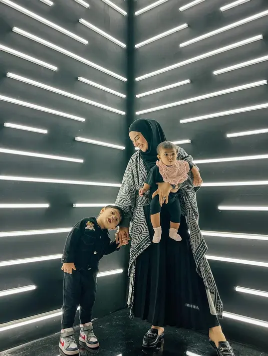 Kali ini, Irish Bella berpose dengan kedua anaknya dengan outfit kompak berwarna hitam. Irish Bella mengenakan pleats skirts hitam dengan outer bermotif hitam-putih, dan hijab simpel berwarna hitam polos. Anak pertamanya mengenakan kemeja dan celana panjang hitam, sedangkan anak keduanya digendong dengan ekspresi gemas mengenakan outfit hitam dan slaber bayi berwarna merah muda. Foto: Instagram.