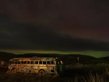 Sebuah aurora borealis, juga dikenal sebagai cahaya utara, terlihat di langit malam saat awan bergerak di atas tengara pinggir jalan yang dikenal sebagai "That NW Bus" di Washtucna, Washington, Amerika Serikat, 27 Februari 2023 dini hari. Berdenyut dalam garis-garis merah, hijau, dan ungu, aurora – juga dikenal sebagai cahaya utara – tampil semarak di belahan bumi utara dari Minggu malam hingga Senin pagi. (AP Photo/Ted S. Warren)