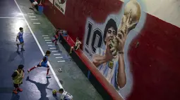Anak-anak bermain sepak bola di dekat mural yang menampilkan mendiang legenda sepak bola dunia, Diego Maradona di klub "Juventud Unida" di Buenos Aires, Argentina, Rabu (24/11/2021). Peringatan pertama kematian Maradona digelar pada 25 November 2021. (AP Photo/Rodrigo Abd)