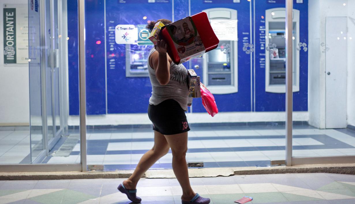 Seorang wanita berjalan usai membawa barang yang ia jarah dari sebuah toko di Veracruz, Meksiko, (4/1). Mereka nekat melakukan aksi vandalisme hingga penjarahan. (AP Photo/Felix Marquez)