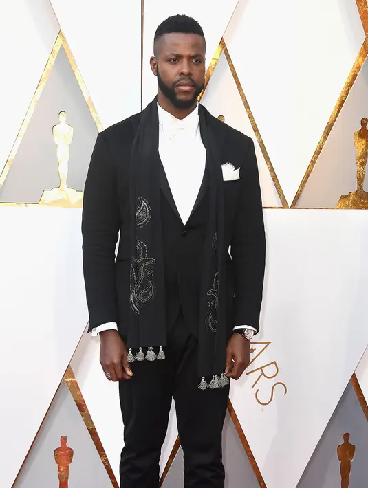 Aktor Winston Duke berpose di karpet merah ajang Piala Oscar 2018, Los Angeles, Minggu (4/3). Pemeran M'Baku dari Black Panther ini mengenakan pakaian serba hitam dengan syal beraksen perak mengkilap. (Frazer Harrison / GETTY IMAGES / AFP)