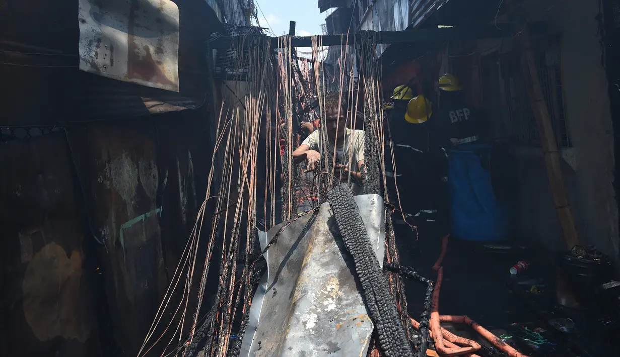 Seorang warga berusaha memotong sisa kabel listrik setelah insiden kebakaran sebuah pemukiman padat penduduk dekat pelabuhan di Manila, Filipina, Selasa (9/5). Mereka berebut mengumpulkan tembaga dari sisa kabel listrik. (TED ALJIBE/AFP)