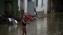 Seorang gadis membawa kursi saat banjir di Itapetinga, negara bagian Bahia, Brasil, Selasa (28/12/2021). Dua bendungan jebol pada Minggu (26/12) di timur laut Brasil, mengancam banjir yang lebih parah di wilayah yang diguyur hujan. (AP/Raphael Muller)