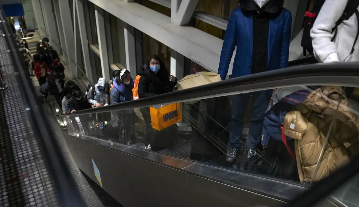 Pelancong yang memakai masker naik eskalator saat mereka tiba dengan penerbangan dari Amerika Serikat di Bandara Internasional Ibukota Beijing di Beijing (9/1/2023). Pelancong internasional pertama tiba di China tanpa karantina wajib yang telah diberlakukan pada awal penerbangan. Pandemi tiga tahun lalu setelah pembatasan dicabut mulai hari Minggu. (AP/Mark Schiefelbein)