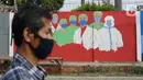 Warga melintas di depan mural bertema covid-19 di Bukit Duri, Jakarta, Minggu (30/8/2020). Mural yang dibuat petugas PPSU bertujuan untuk mengingatkan masyarakat akan bahaya covid-19, sehubungan dengan masih tingginya jumlah kasus positif covid-19 di Jakarta. (Liputan6.com/Immanuel Antonius)