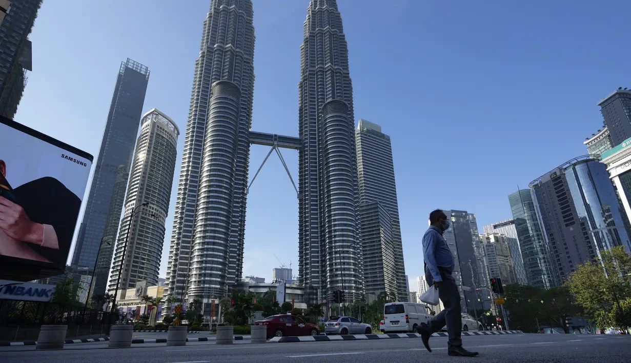 Seorang pria yang mengenakan masker berjalan di sepanjang jalan kosong di depan Menara Kembar pada hari pertama Full Movement Control Order (MCO) di Kuala Lumpur, Malaysia, Selasa (1/6/2021). (AP Photo/Vincent Thian)