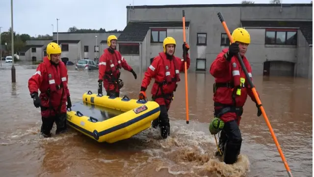 Petugas penyelamat penjaga pantai berjalan melalui jalan yang banjir untuk mengevakuasi orang-orang yang terjebak di rumah di Brechin, timur laut Skotlandia, pada 20 Oktober 2023 saat Badai Babet melanda negara itu. (AFP/Andy Buchanan)