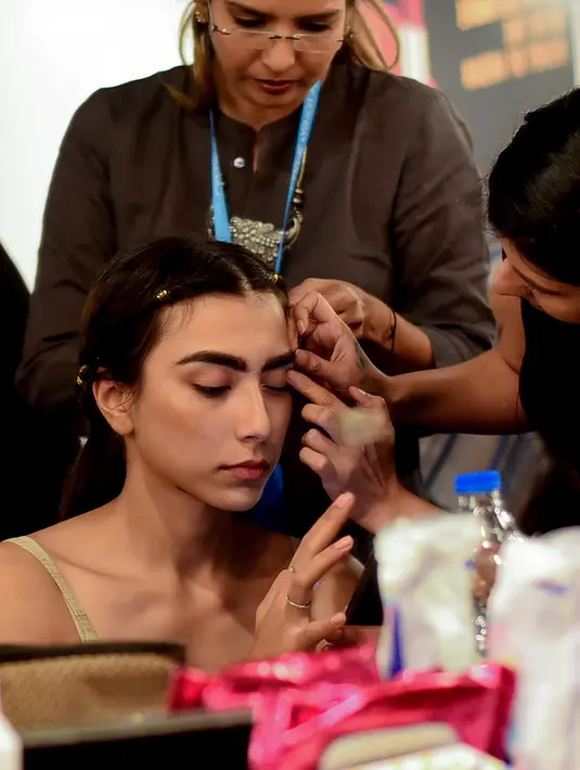 Seorang model India saat dirias oleh kru makeup di belakang panggung sebelum tampil di catwalk selama Lakmé Fashion Week (LFW) Summer Resort 2019 di Mumbai, India (31/1). (AFP Photo/Sujit Jaiswal)