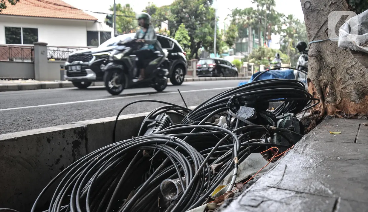 Kendaraan melintas di dekat jaringan kabel utilitas yang menjuntai di Jalan Proklamasi, Pegangsaan, Kecamatan Menteng, Jakarta Pusat, Kamis (6/10/2022). Minimnya pengawasan dalam tahap penyelesaian proyek revitalisasi trotoar oleh pihak terkait menyebabkan jaringan kabel utilitas di kawasan tersebut semrawut  yang dapat membahayakan keselamatan pengguna jalan, terutama saat musim penghujan. (merdeka.com/Iqbal S. Nugroho)