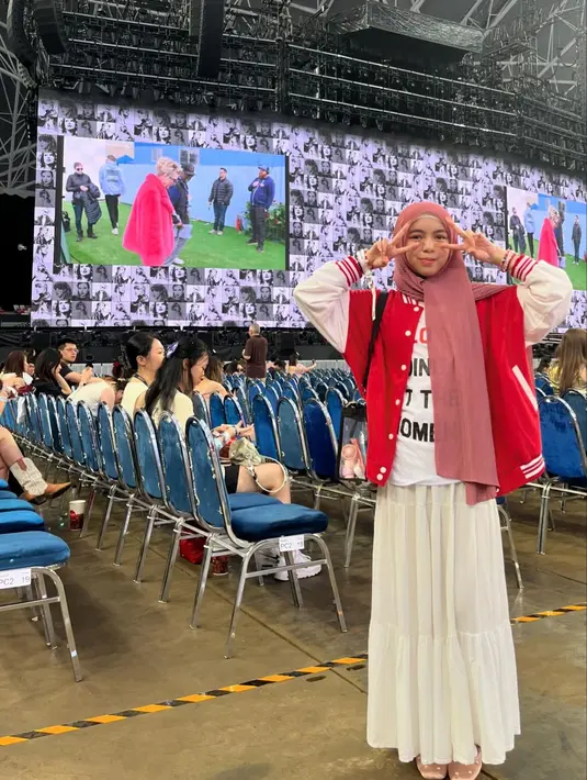 Gaya chic Sienna saat menonton konser Taylor Swift. Ia mengenakan kaus berwarna dasar putih dengan corak tulisan ditumpuk baseball jacket merah, dan rok panjang berwarna putih, serta hijab pink polos. [Foto: Instagram/siennn.kasya]