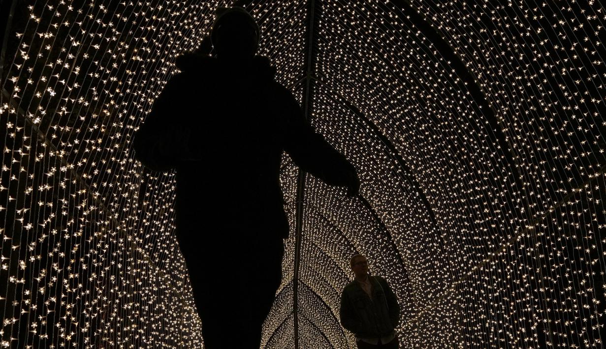 Orang-orang berjalan melalui terowongan lampu bagian dari instalasi cahaya yang dipamerkan menyambut Natal di Royal Botanic Gardens, Kew, London, Selasa (15/11/2022). Selain memamerkan jalur cahaya dengan satu juta lampu di jalur sepanjang 2,7 km, terdapat cahaya imersif, pohon lampu, terowongan cahaya, dan pertunjukkan cahaya air yang mengesankan. (AP Photo/Kirsty Wigglesworth)