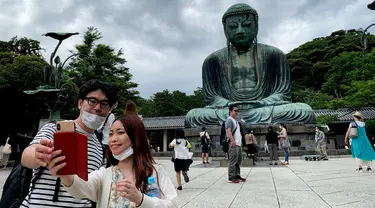 Sepasang pengunjung berswafoto dengan latar belakang The Great Buddha atau yang biasa disebut Kamakura Daibutsu di kuil Kotoku-in di Kamakura, Prefektur Kanagawa, Jepang, Sabtu (20/6/2020). Patung Buddha yang menjulang dengan tinggi 13,35 meter ini didirikan tahun 1252. (Behrouz MEHRI/AFP)