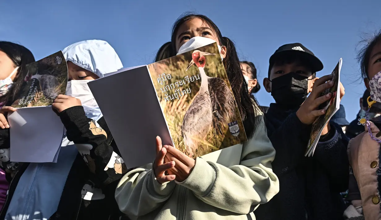 Anak-anak sekolah berkumpul untuk menyaksikan pelepasan bangau Sarus Timur yang dibiakkan di di waduk Huai Chorakhe Mak, Buriram, Thailand, Minggu (25/12/2022). Burung bangau yang satu ini hampir menghilang dari Thailand saat 50 tahun lalu. (Lillian SUWANRUMPHA / AFP)