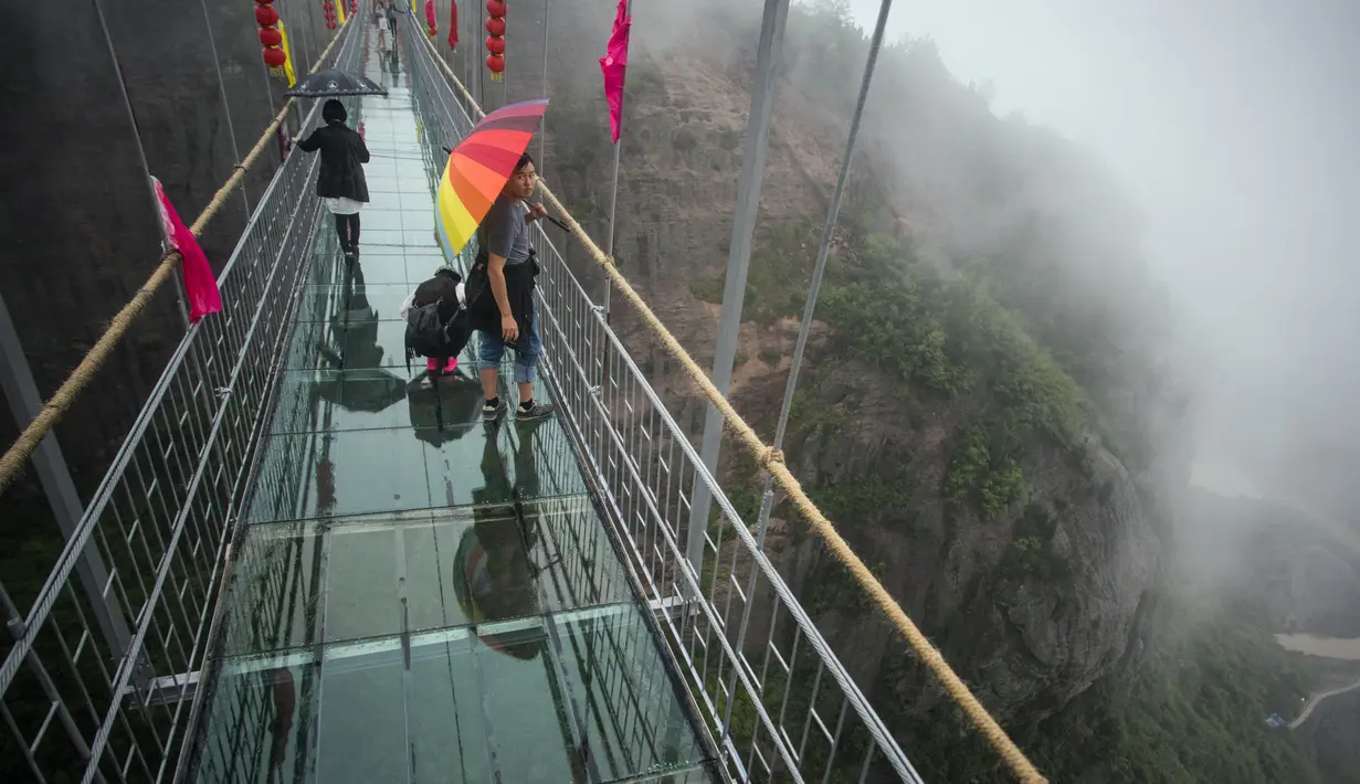 Wisatawan berjalan di jembatan gantung yang terbuat dari kaca di pegunungan Shinuizhai, Provinsi Hunan, Tiongkok, 6 Oktober 2015. Jembatan dengan panjang 300 m dan tinggi 180 m ini kembali dibuka setelah direnovasi untuk objek wisata.(AFP/Johannes Eisele)