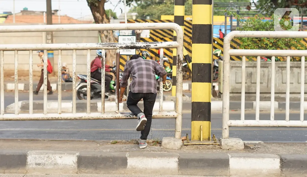 Warga menerobos celah pagar pembatas jalan di depan Stasiun Pasar Minggu, Jakarta, Rabu (16/10/2019). Jauhnya jembatan penyeberangan orang (JPO) membuat warga memanfaatkan celah pagar pembatas tersebut sebagai akses menyeberang, meski berbahaya bagi keselamatan. (Liputan6.com/Immanuel Antonius)