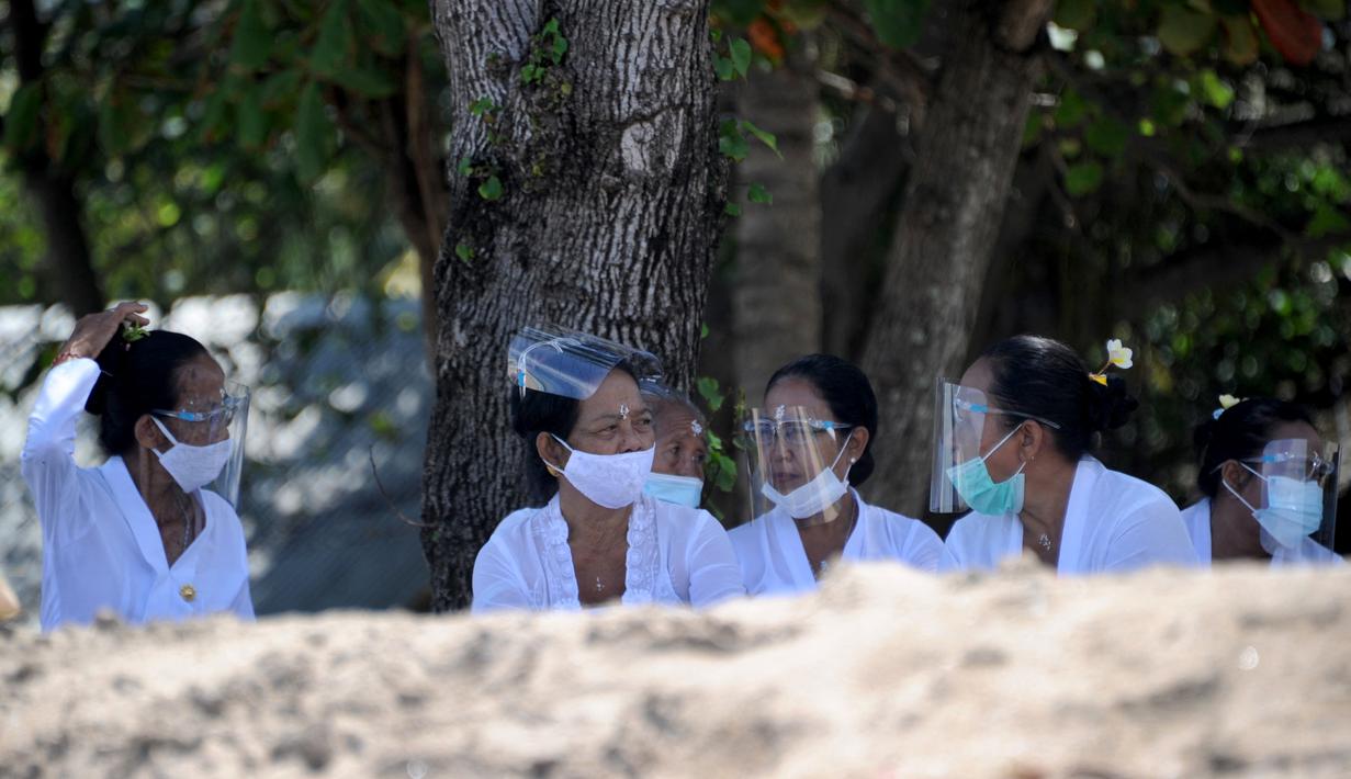 Umat Hindu mengenakan face shield menghadiri upacara Melasti menjelang Hari Raya Nyepi di Pantai Kuta, Bali (11/3/2021). Upacara Melasti dilakukan oleh perwakilan desa adat dengan jumlah terbatas serta menerapkan protokol kesehatan untuk mencegah penyebaran pandemi COVID-19. (AFP/Sonny Tumbelaka)