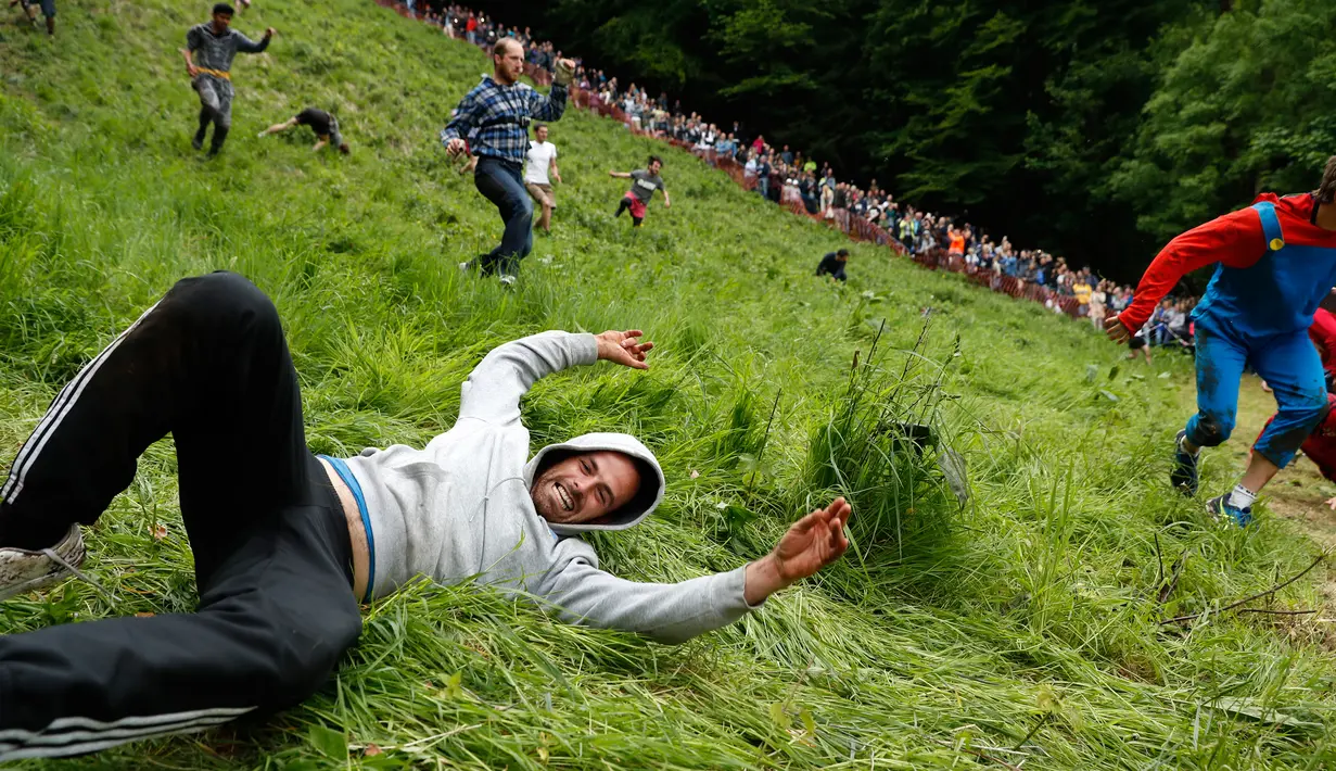 Ekspresi peserta yang jatuh saat mengejar gulungan keju dalam kompetisi Cheese Rolling di Brockworth, Gloucestershire, Inggris, 30 Mei 2016. Persaingan dimulai setelah keju yang berbentuk seperti roda digelindingkan dari puncak bukit. (Adrian DENNIS/AFP)
