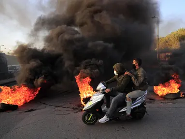 Pengunjuk rasa melewati ban yang dibakar untuk memblokir jalan raya menuju bandara internasional Beirut, Selasa (2/3/2021). Warga Lebanon yang marah memblokir jalan setelah mata uang Lebanon jatuh ke titik terendah baru dalam krisis keuangan yang memicu kemiskinan. (AP Photo/Hussein Malla)