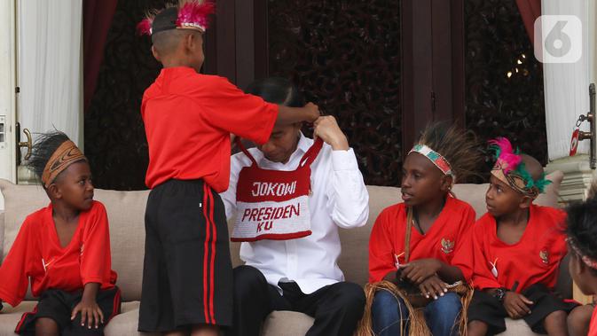 Presiden Joko Widodo atau Jokowi mendapatkan hadiah dari perwakilan anak-anak sekolah dasar Papua di Istana Merdeka, Jakarta, Jumat (11/10/2019). Pertemuan Jokowi dengan perwakilan anak-anak SD dari Papua digelar dalam suasana santai di beranda belakang Istana Merdeka. (Liputan6.com/Angga Yuniar)