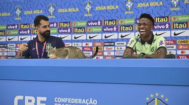 Seekor kucing naik ke meja saat penyerang Brasil #20 Vinicius Junior yang tertawa memberikan konferensi pers sesi konferensi pers Vinicius Junior jelang Kroasia vs Brasil pada perempat final Piala Dunia 2022, di Stadion Al Arabi SC di Doha, Rabu (7/12/2022). Saat sesi tanya jawab tengah berlangsung, tamu tak diundang yakni seekor kucing ikut menimbrung. (NELSON ALMEIDA / AFP)