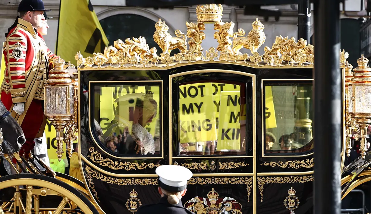 Raja Inggris Charles III dan Ratu Inggris Camilla melakukan perjalanan dengan Diamond Jubilee State Coach melewati para pengunjuk rasa yang memegang plakat "Not My King" dari kelompok anti-monarki Republik saat mereka berdemonstrasi menjelang Pembukaan Parlemen, di seberang Gedung Parlemen di London pada 7 November 2023. (HENRY NICHOLLS/AFP)