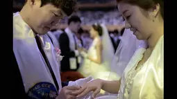Mempelai pria tampak memasangkan cincin kawin kepada mempelai wanitanya saat acara pernikahan massal yang diselenggarakan oleh Gereja Unifikasi di Gapyeong, Korea Selatan, Selasa (3/2/2015). (AFP PHOTO/Ed Jones)