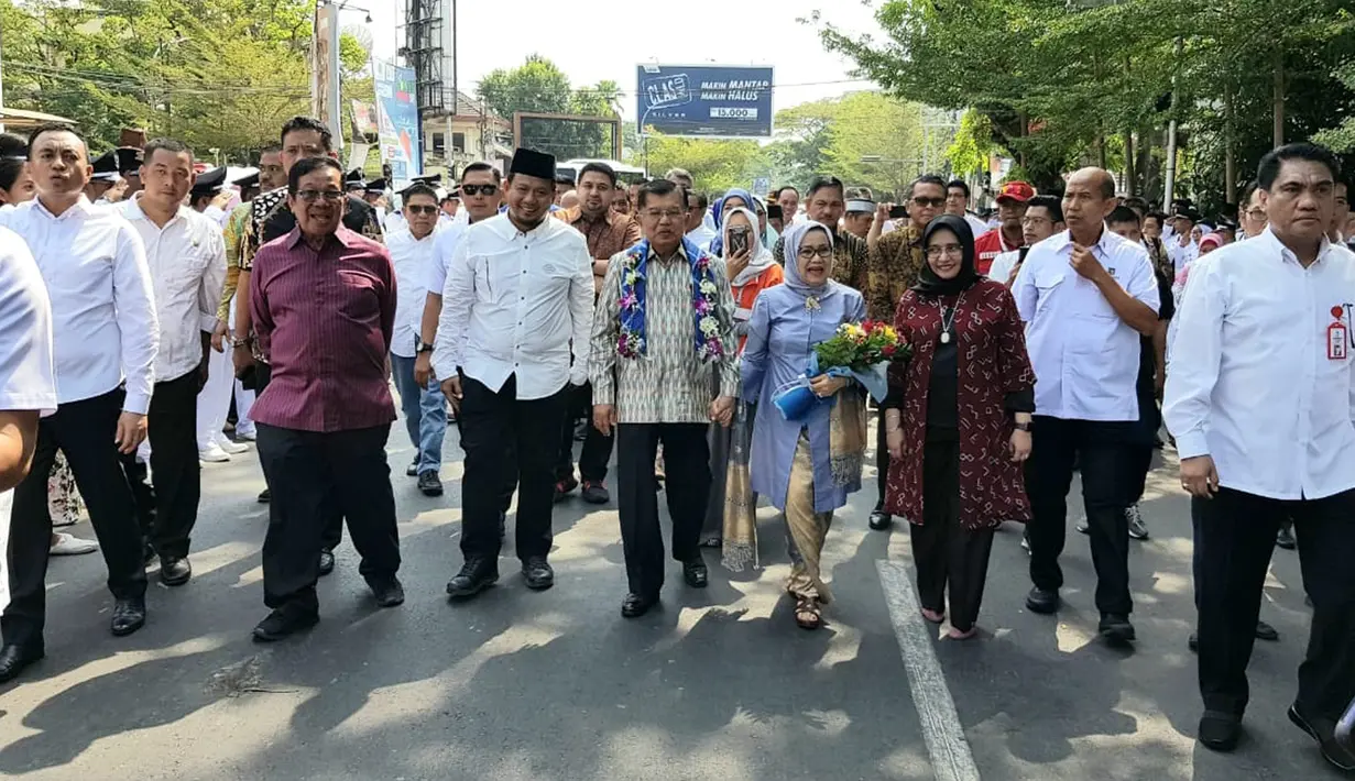 Mantan Wakil Presiden Jusuf Kalla atau JK didampingi istrinya Mufidah berjalan kaki saat tiba di kampung halamannya, Makassar, Sulawesi Selatan, Sabtu (26/10/2019). Beragam pertunjukan ditampilkan saat JK dan rombongan berjalan. (Liputan6.com/HO/Tim JK)