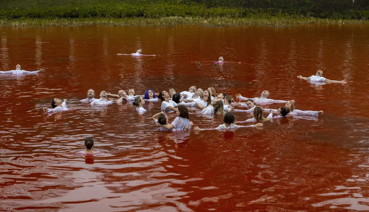 Orang-orang mandi dalam kolam warna merah untuk menandakan darah, selama protes terhadap invasi Rusia ke Ukraina di depan kedutaan besar Rusia di Vilnius, Lithuania, Kamis (7/4/2022). Protes tersebut menyoroti ancaman genosida dari operasi militer Rusia. (AP Photo/Mindaugas Kulbis)