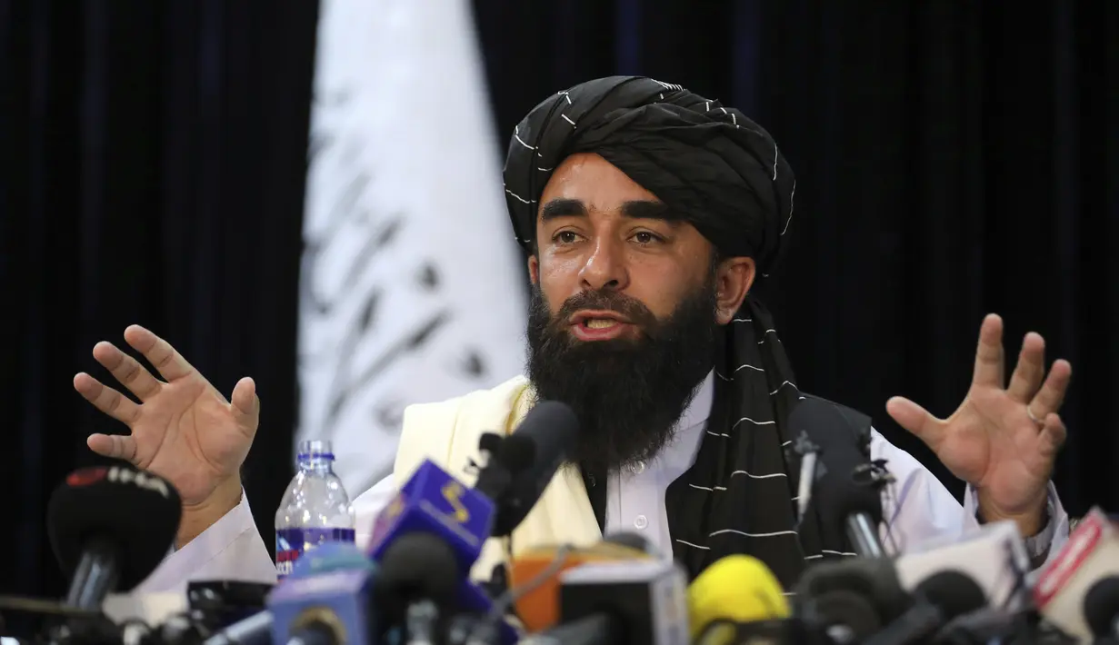 Di depan bendera Taliban, juru bicara Taliban Zabihullah Mujahid berbicara pada konferensi pers pertamanya, di Kabul, Afghanistan, pada Selasa (17/8/2021). Mujahid menjawab berbagai pertanyaan dari wartawan dalam konferensi pers bersejarah. (AP Photo/Rahmat Gul)