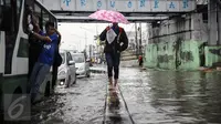 Seorang pejalan kaki sambil menggunakan payung melintasi banjir yang menggenangi jalan di depan Ancol, Jakarta, Kamis (21/4). Hujan deras yang mengguyur sejak semalam menyebabkan beberapa kawasan di Jakarta tergenang banjir. (Liputan6.com/Faizal Fanani) 